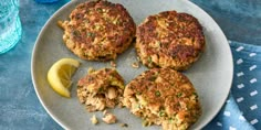 three crab cakes on a plate with lemon wedges