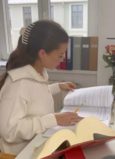 a woman sitting at a desk with an open book in front of her and writing