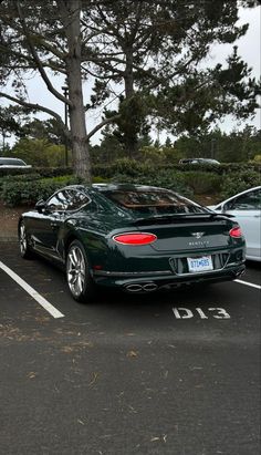 a green sports car parked in a parking lot next to two white cars and trees