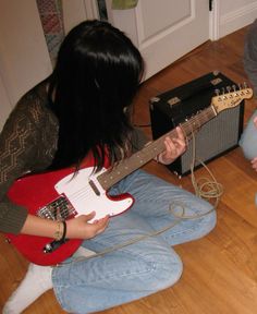 two people are sitting on the floor playing guitar and another person is holding an electric guitar