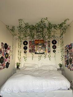 a white bed with lots of pictures on the wall above it and plants growing from the headboard