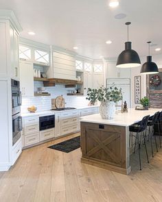 a large kitchen with white cabinets and wooden flooring, along with black pendant lights hanging from the ceiling