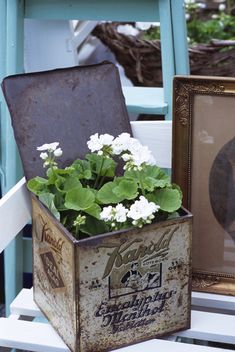 an old metal box with flowers in it sitting on a chair next to a framed photo