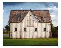 an old white barn sitting in the middle of a field