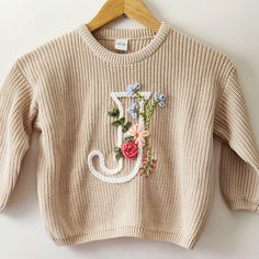 a sweater with flowers is hanging on a hanger and it has the letter j painted on it