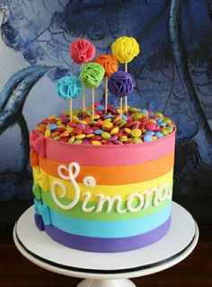 a rainbow cake with candies on top and the word simona spelled in white