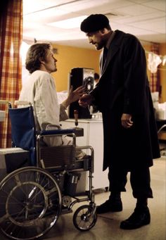 a man standing next to a woman in a room with a wheel chair on the floor