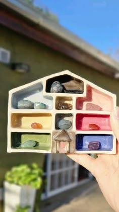 a person holding up a small house made out of different colored rocks