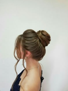 a woman with her hair in a high ponytail, wearing a blue dress and standing against a white wall