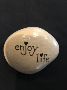 a rock with the words enjoy life written on it and hearts in black ink, sitting on a black surface