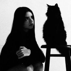 a black and white photo of a woman sitting in front of a cat on a stool