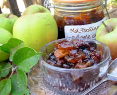 apples and raisins in a glass bowl on a plate with spoons next to them