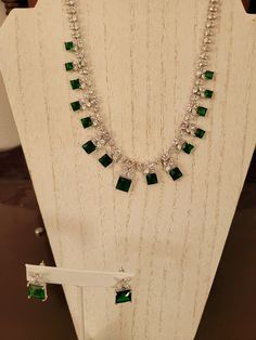 "The necklace has square cut emeralds that are one to six carats each for a total of 38 carats emerald.  The chain is done in 1mm round and square cut diamonds with 3mm diamond petal design above the emeralds.  It has 5 carats of diamond accents.    It is a non adjustable 16 inches with a fold over clasp closure.  The earrings are pierced and have a 5 carat square cut emerald stone with an \"x\" design .66 carat diamond accents.  Platinum plated." Formal White Gold Emerald Necklace With Jewels, Fine Jewelry Emerald Cut Emerald Necklace For Formal Events, Diamond White Emerald Cut Jewelry For Formal Events, Formal Emerald Necklaces With Diamond Cut, Emerald Cut Diamond White Jewelry For Formal Occasions, Emerald Cut Diamond White Jewelry For Formal Events, Luxury Square Cut Emerald Jewelry, Formal Diamond White Emerald Cut Jewelry, Elegant Emerald Necklace For Formal Occasion