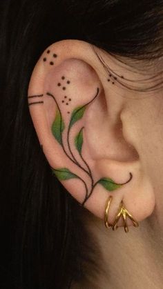 a woman's ear with green leaves and stars on it, behind her ear