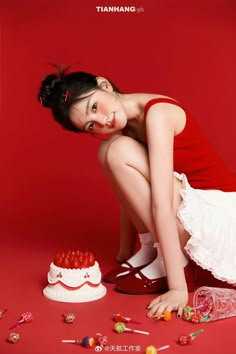 a woman kneeling down next to a cake and candies on the ground with her legs crossed