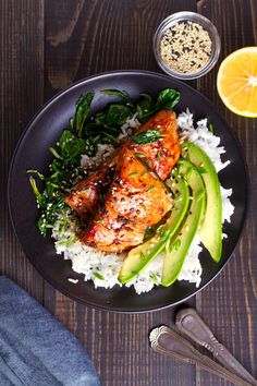 a black plate topped with chicken, rice and veggies next to an orange slice