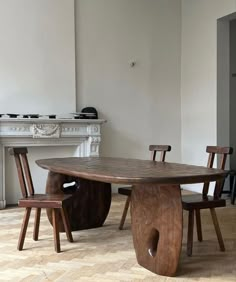 a wooden table with chairs around it in front of a fire place and white walls