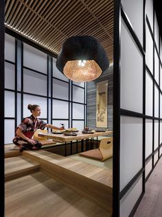 a woman sitting at a table in a room with wood floors and large glass windows