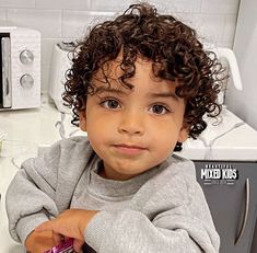 a little boy sitting on top of a sink next to a hair dryer and comb