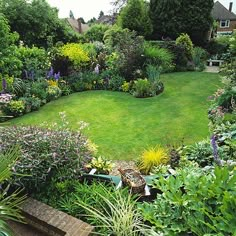 a lush green yard with lots of flowers and plants around the perimeter, surrounded by greenery