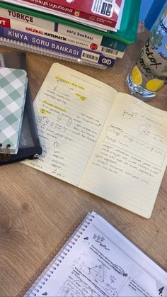 several books are stacked on top of each other next to a glass of water and notebooks