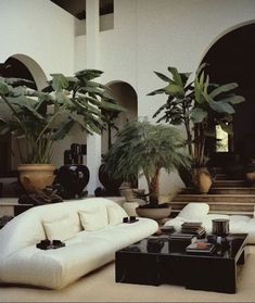 a living room filled with white furniture and potted plants on top of it's tables