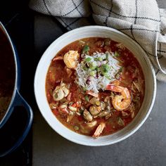 a white bowl filled with shrimp and rice next to a pot of soup on top of a table