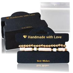 two bracelets with white and gold beads are in front of a black gift box