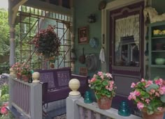 a porch with potted plants and flowers on the front steps, next to a purple bench