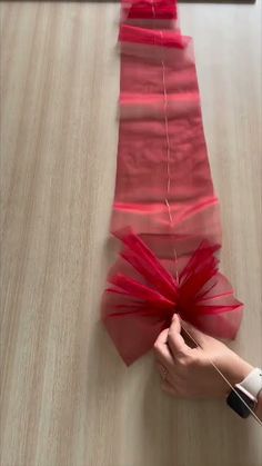 someone is making a piece of red organe ribbon on a table with scissors and thread