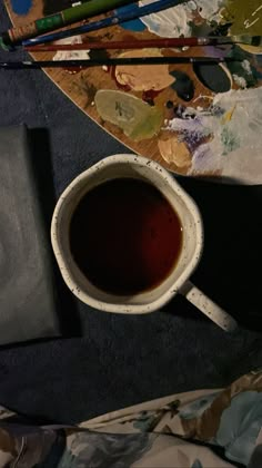 a cup of tea sitting on top of a table next to some paintbrushes