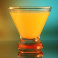 a glass filled with yellow liquid sitting on top of a reflective countertop next to a blue and green background