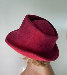 This one of a kind felted hat was made of Merino and Bergschaf wool. The main colours are red, burgundy and black. The hat was made in one piece on a resist. The resist was covered with wool fibres, which were manually rolled for many hours using only warm soapy water. The felted cone was further  manipulated into a fedora hat shape. The hat is water repellent and great for travelling as it will retain its shape even when folded flat in a bag or a suitcase. For care instructions please refer to