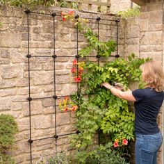 a woman standing next to a brick wall with flowers growing on it