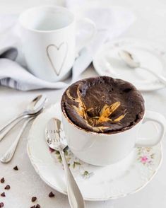 a chocolate dessert in a white cup on a saucer with spoons next to it