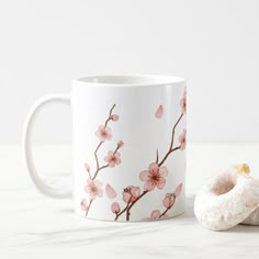 a doughnut sitting next to a coffee mug with pink flowers and leaves on it