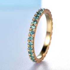 a gold ring with blue and green stones on the inside, sitting on a white surface