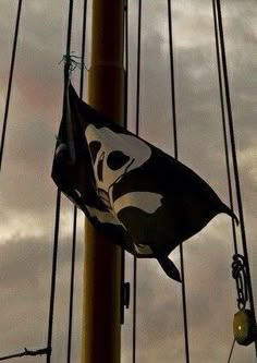 a pirate flag hanging from the side of a tall pole with other masts in the background