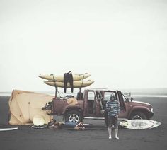 a man standing next to a truck with surfboards on top of it