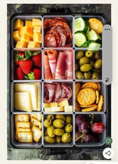 an open lunch box filled with cheese, crackers, fruit and meats on top of each other