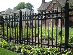 an iron fence in front of a brick house with green plants growing on the side