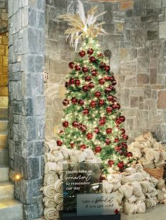 a christmas tree is decorated with red and white ornaments in front of a stone wall