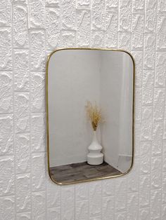 a white vase sitting on top of a wooden table next to a wall mounted mirror