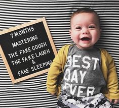 a baby laying on top of a bed next to a sign