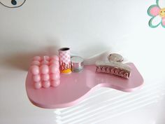 there is a pink shelf on the wall with some items in front of it,