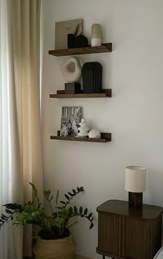 two wooden shelves on the wall above a table with a lamp and potted plant