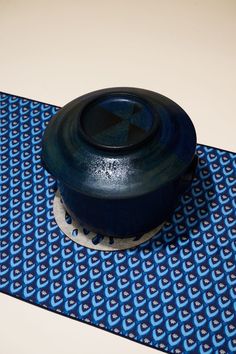 a blue and white patterned table mat with a black lid on it, sitting on top of a floor