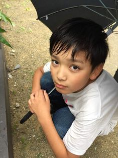 a young boy sitting on the ground with an umbrella over his head and looking at the camera