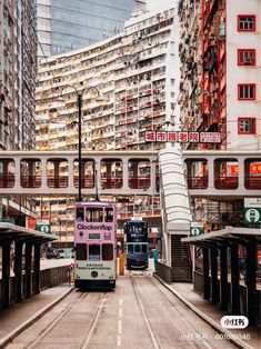 two double decker buses driving down the street in front of tall buildings with red and white signs