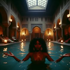 a woman sitting in the middle of a pool with her hands out and lights on